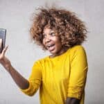 A cheerful woman with curly hair takes a selfie indoors, capturing happiness and technology.